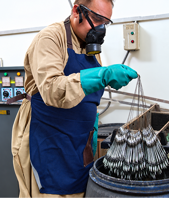 Worker in protective gear dipping surgical instruments into a treatment tank