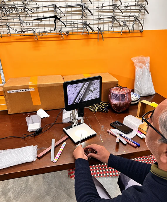 Technician inspecting surgical instruments under a digital microscope
